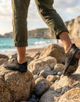 Person wearing aqua shoes walking on rocky beach showing strong grip and non slip performance on wet surfaces