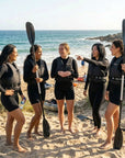 Group of women wearing Baltic Aqua Pro black canoe buoyancy aids standing on a sandy beach with kayak paddles before launching for kayaking on the sea.