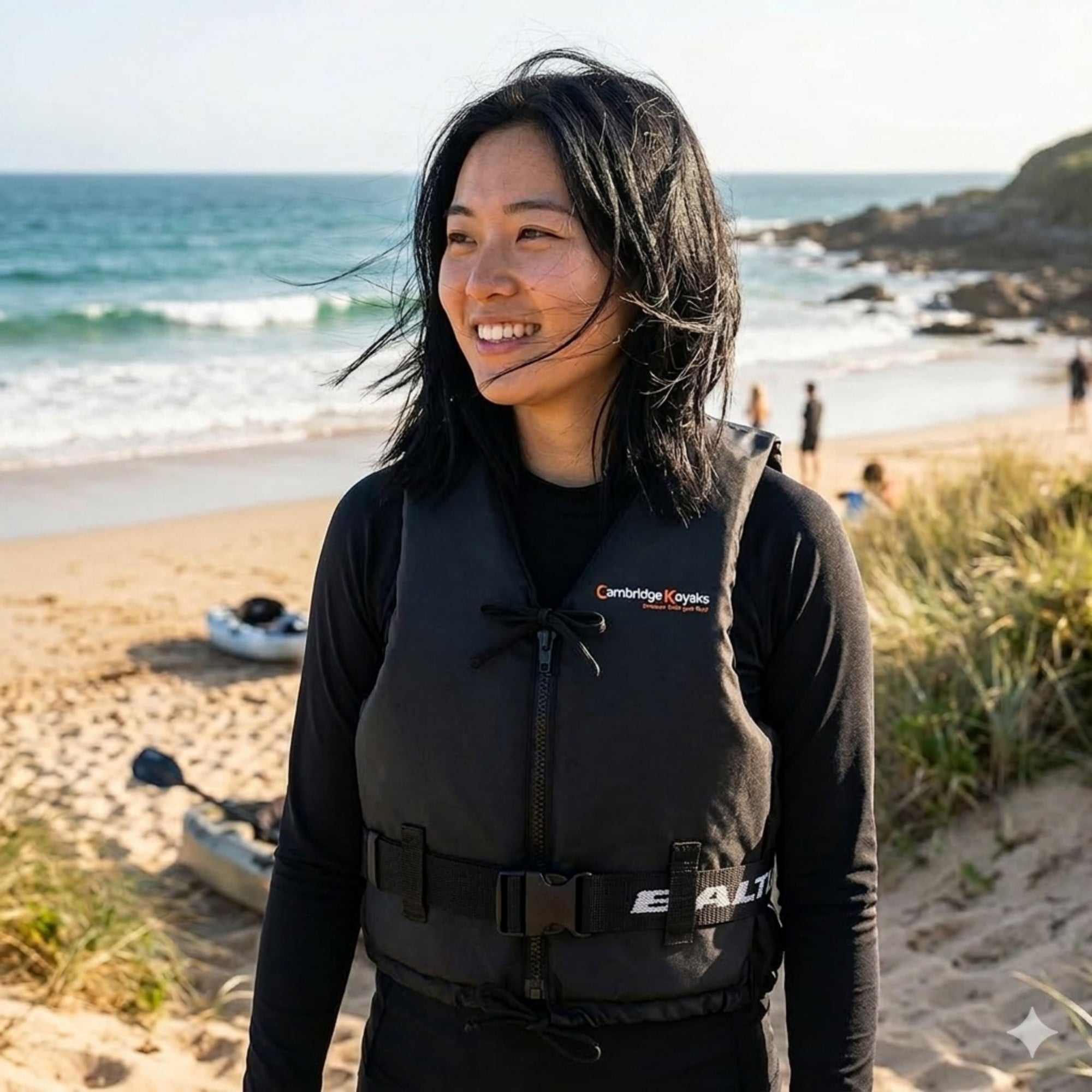 Woman standing on a sandy beach wearing Baltic Aqua Pro black canoe buoyancy aid with front zip fastening and adjustable waist belt for kayaking, canoeing, and paddle sports.