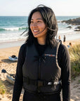 Woman standing on a sandy beach wearing Baltic Aqua Pro black canoe buoyancy aid with front zip fastening and adjustable waist belt for kayaking, canoeing, and paddle sports.