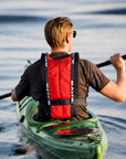 Rear view of kayaker paddling in a green kayak wearing Baltic canoe buoyancy aid showing reinforced back panel, adjustable safety belt, and ergonomic design for comfort and freedom of movement