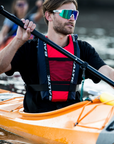 Kayaker wearing Baltic canoe buoyancy aid in red with reinforced shoulder straps, adjustable waist belt, and breathable mesh front pocket while paddling an orange kayak on open water