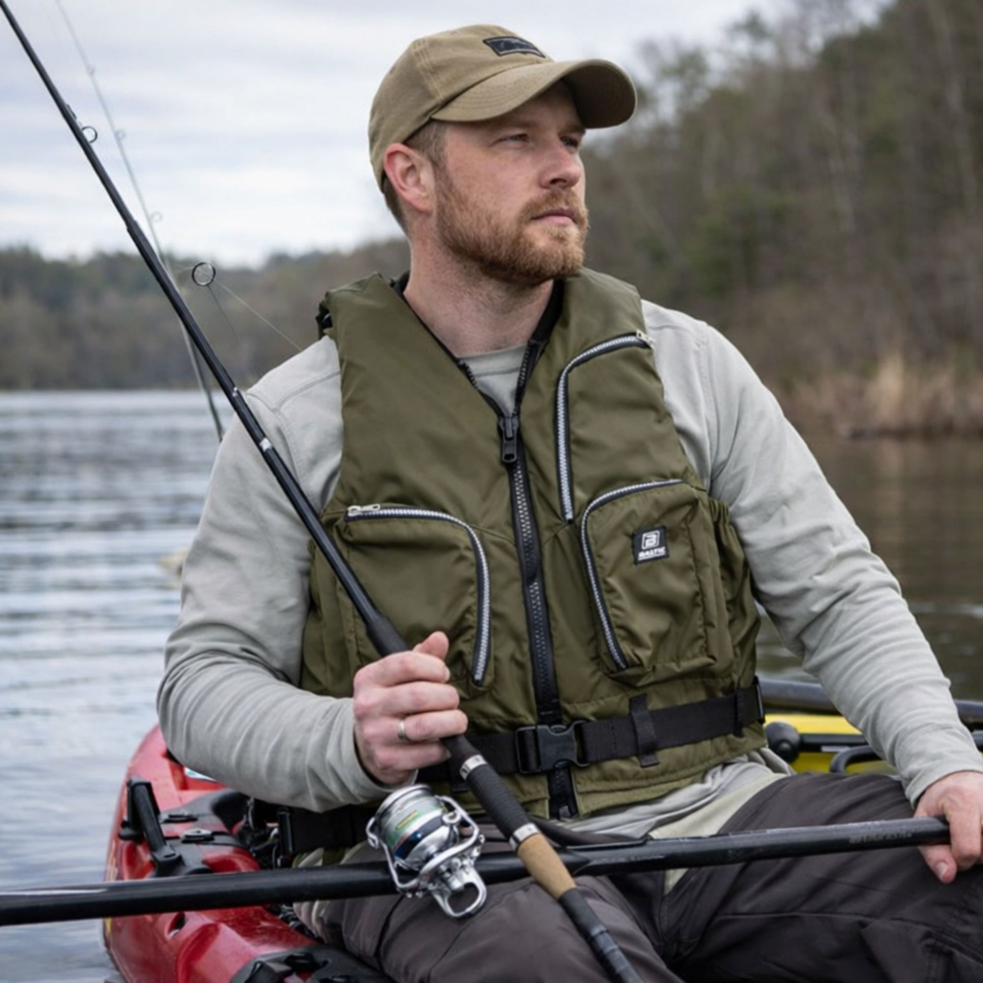 Close view of Baltic Outdoor camo green buoyancy aid showing zipped storage pockets, front zip fastening, and adjustable waist belt worn by kayak fisherman