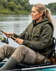 Female kayak angler wearing Baltic Outdoor camo green buoyancy aid with large storage pockets while fishing from a seated kayak on a river