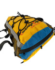 Front angled view of the Cambridge Kayaks yellow and blue Access Deck Bag showing the bungee cord top, side mesh pockets, and multiple securing straps for easy kayak attachment.