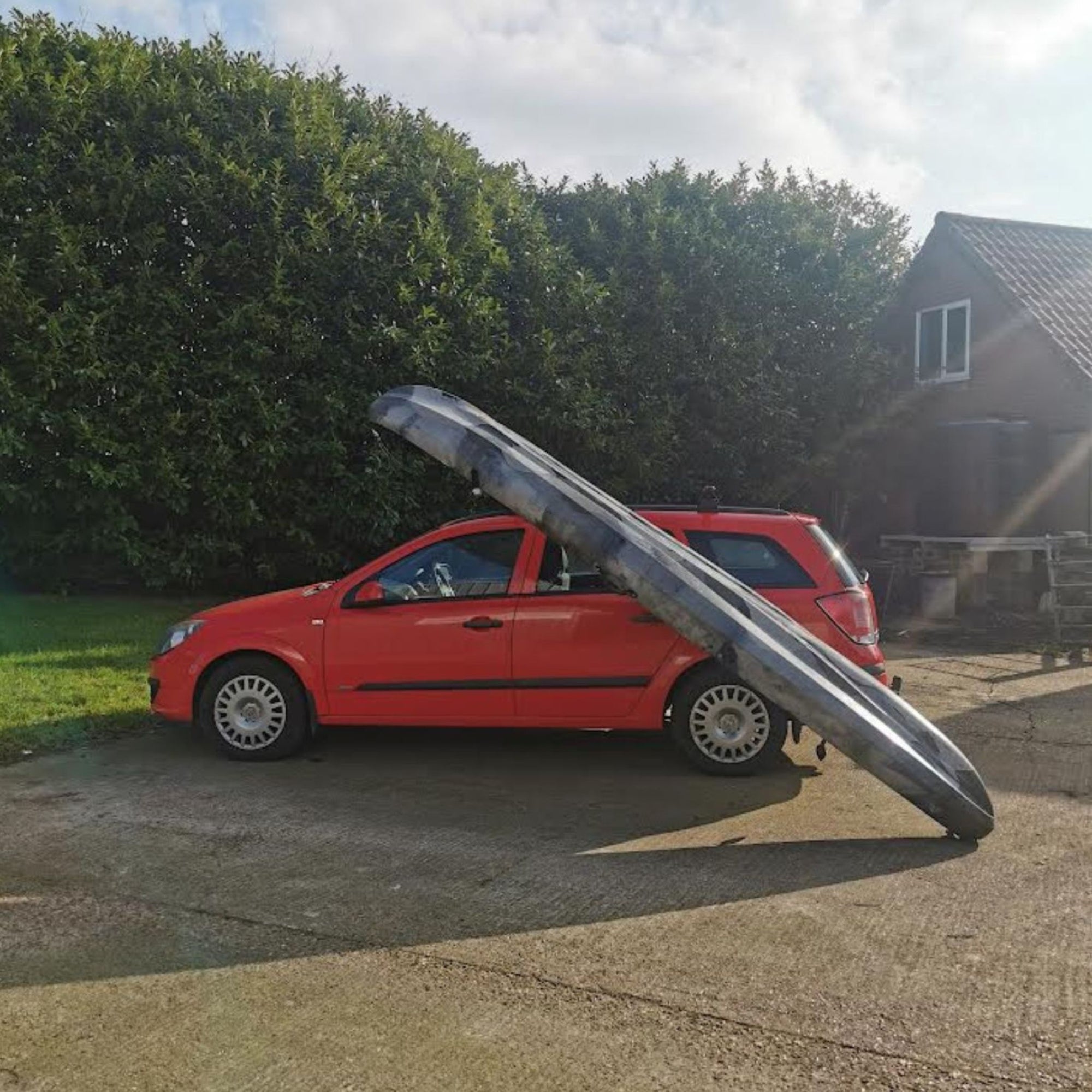 Side view of the Cambridge Kayaks Load Assisting Rack Bar in use, with a red car and grey camouflage kayak illustrating lift-assist functionality.