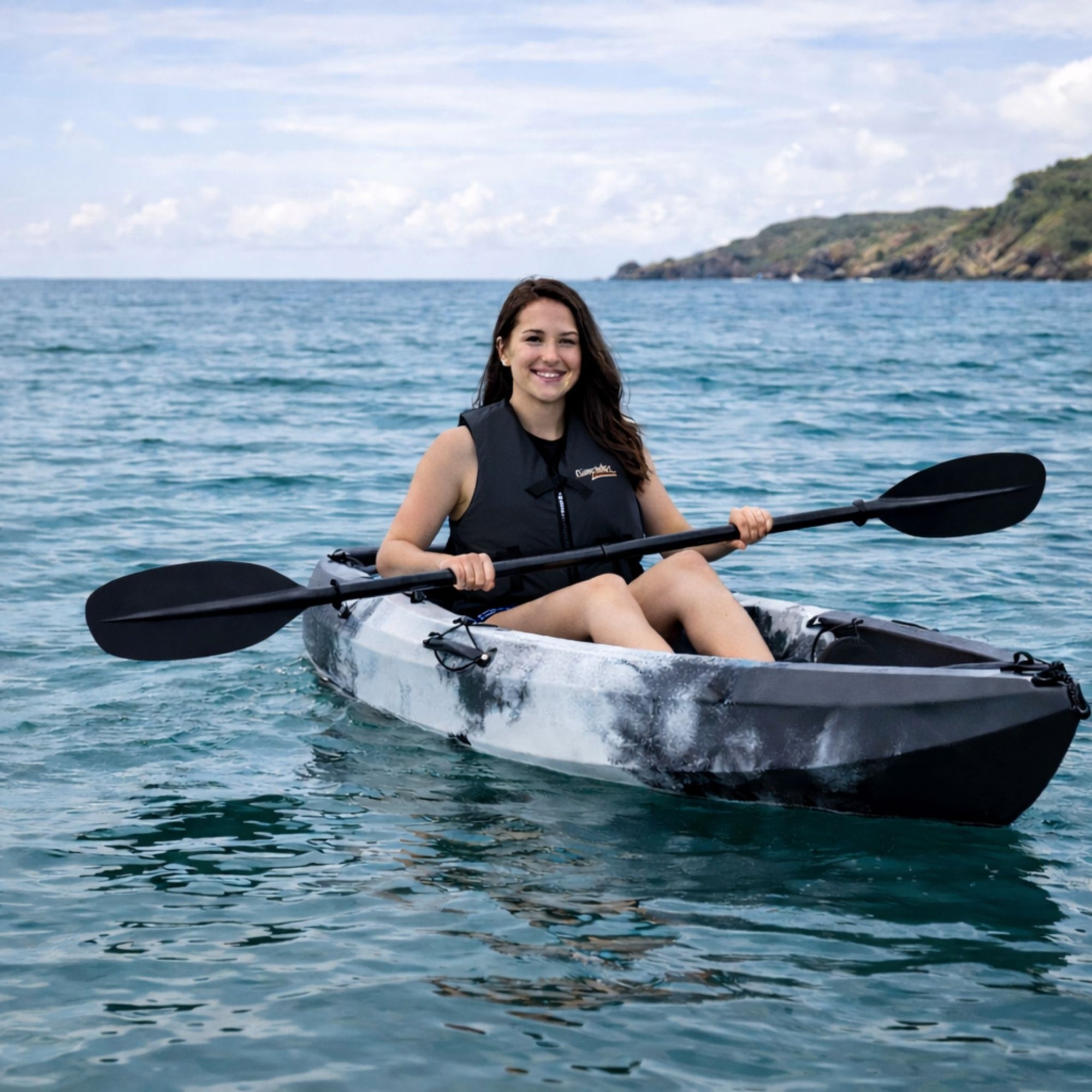 Woman paddling Cambridge Kayaks Neptune single sit on top kayak on calm sea near coastline