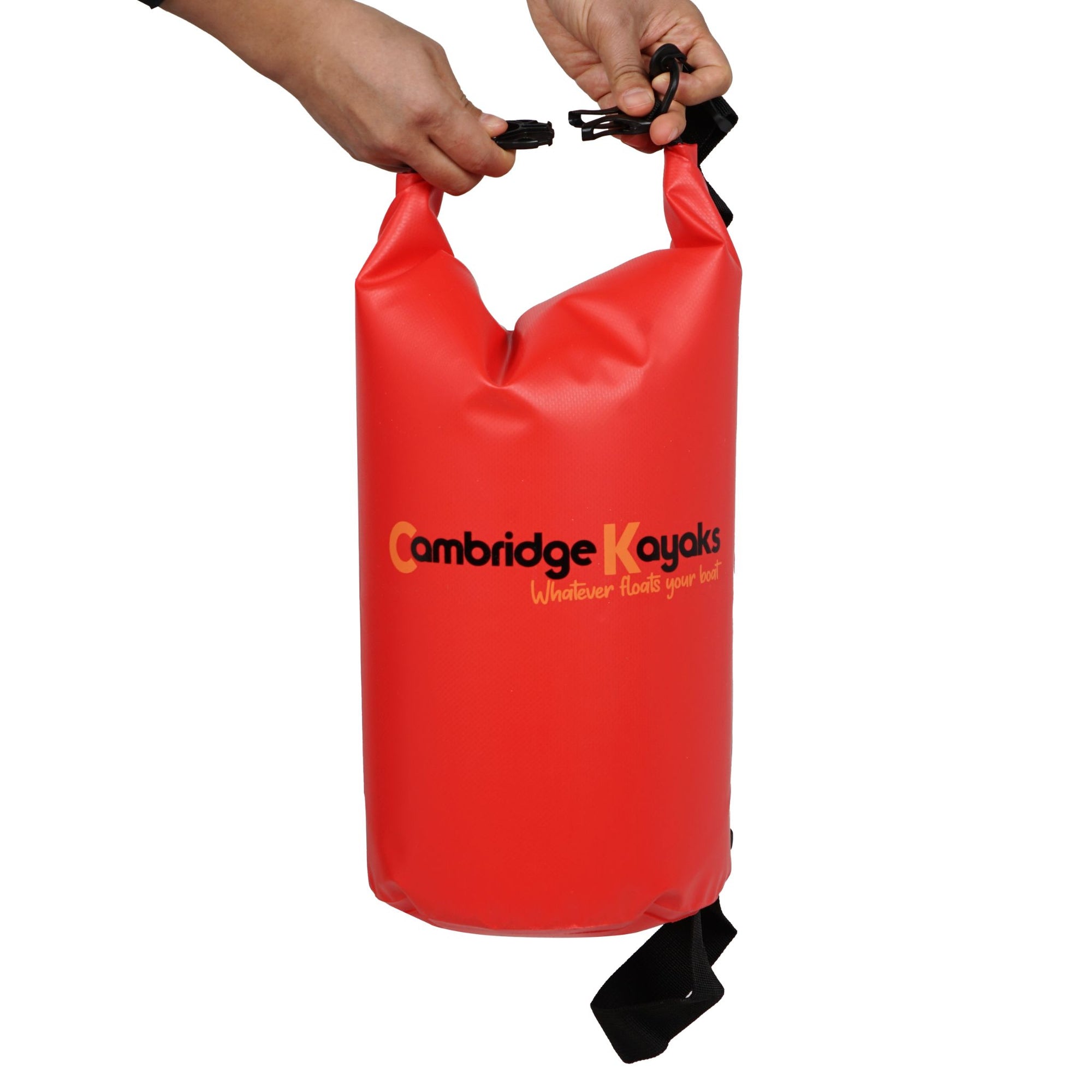 Close-up shot of a red Cambridge Kayaks dry bag being held by its black buckle strap, highlighting the lightweight PVC construction and watertight sealing system.