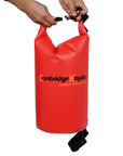 Close-up shot of a red Cambridge Kayaks dry bag being held by its black buckle strap, highlighting the lightweight PVC construction and watertight sealing system.