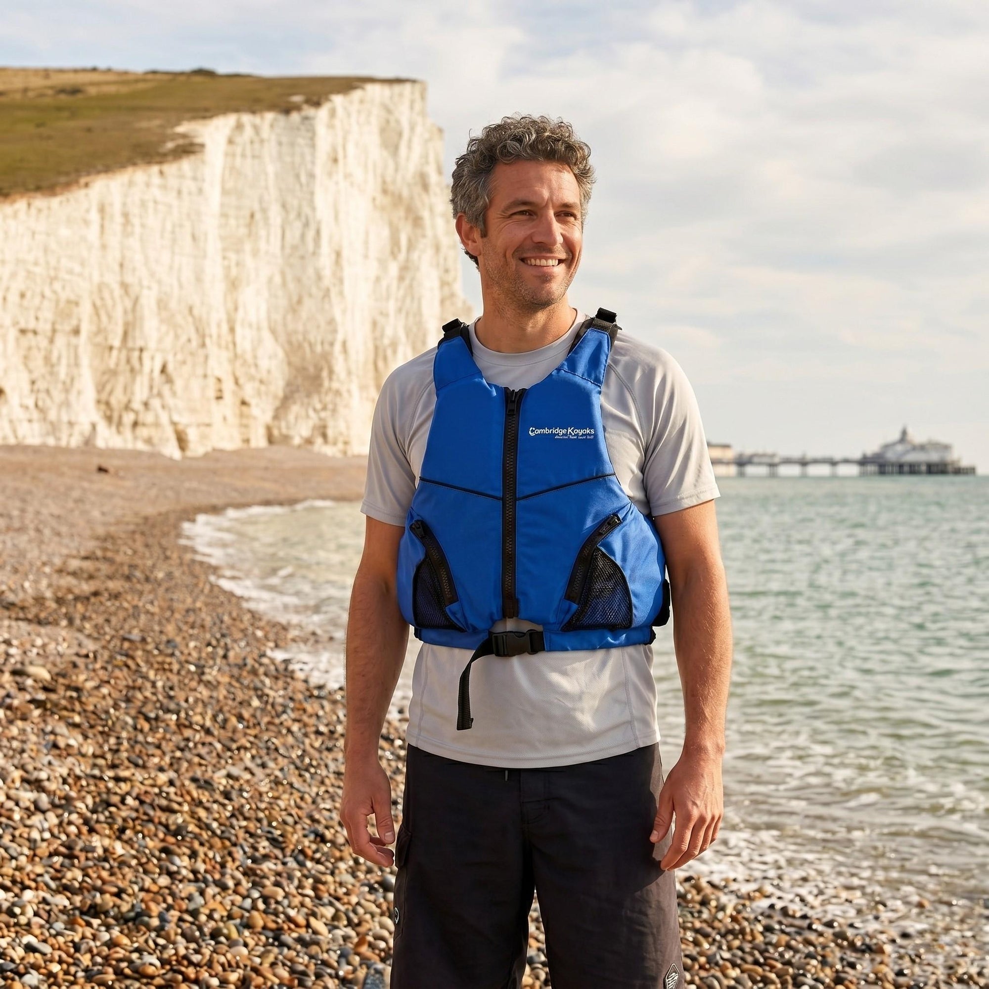 Man wearing blue Cambridge Kayaks buoyancy aid on pebble beach beside the sea