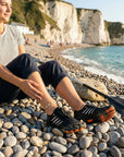 Woman wearing water shoes on pebble beach showing strong grip and non slip sole for coastal walking and water activities