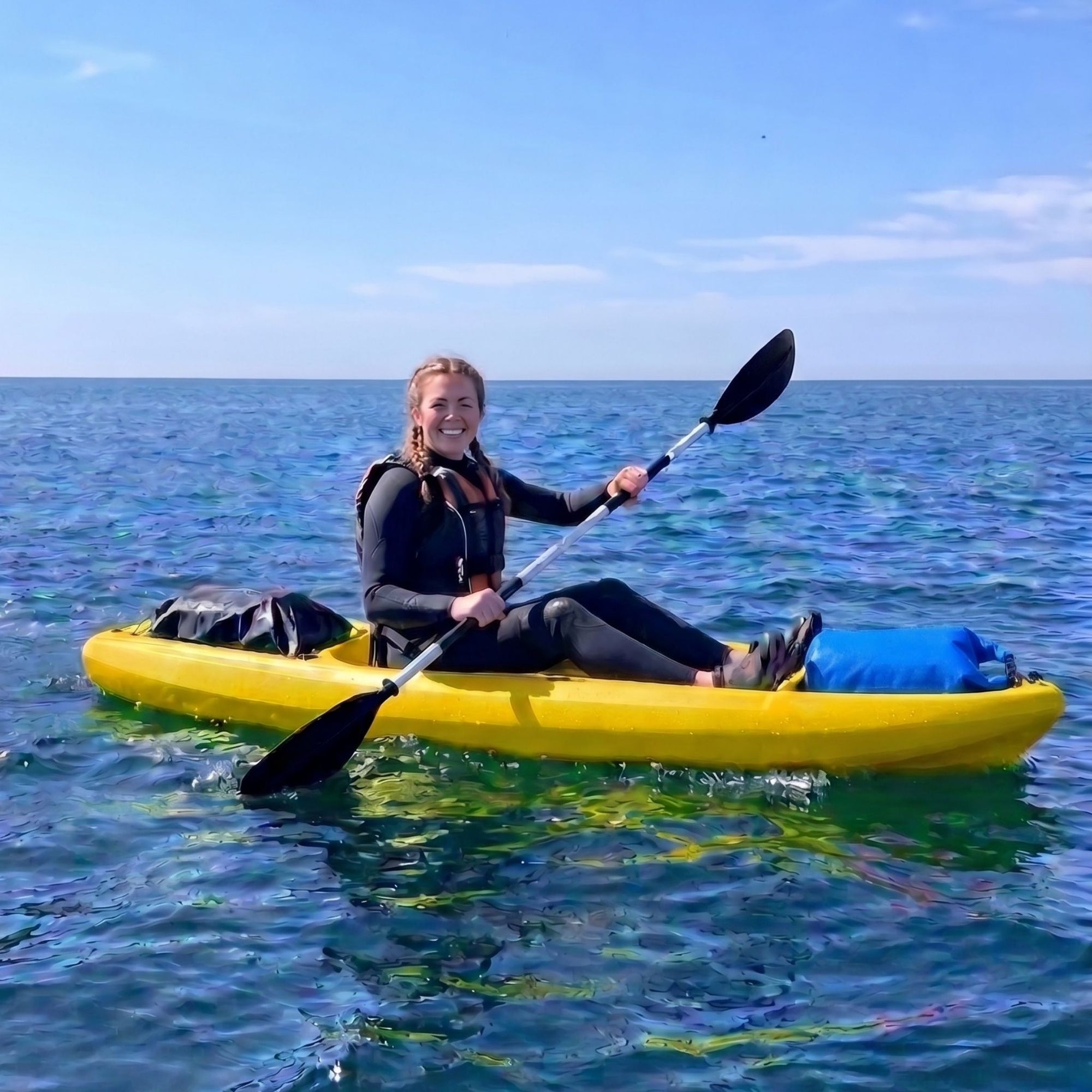 Person paddling single sit on top kayak on open water under blue sky