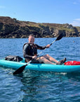 Man paddling single sit on top kayak on clear sea near rocky coastline