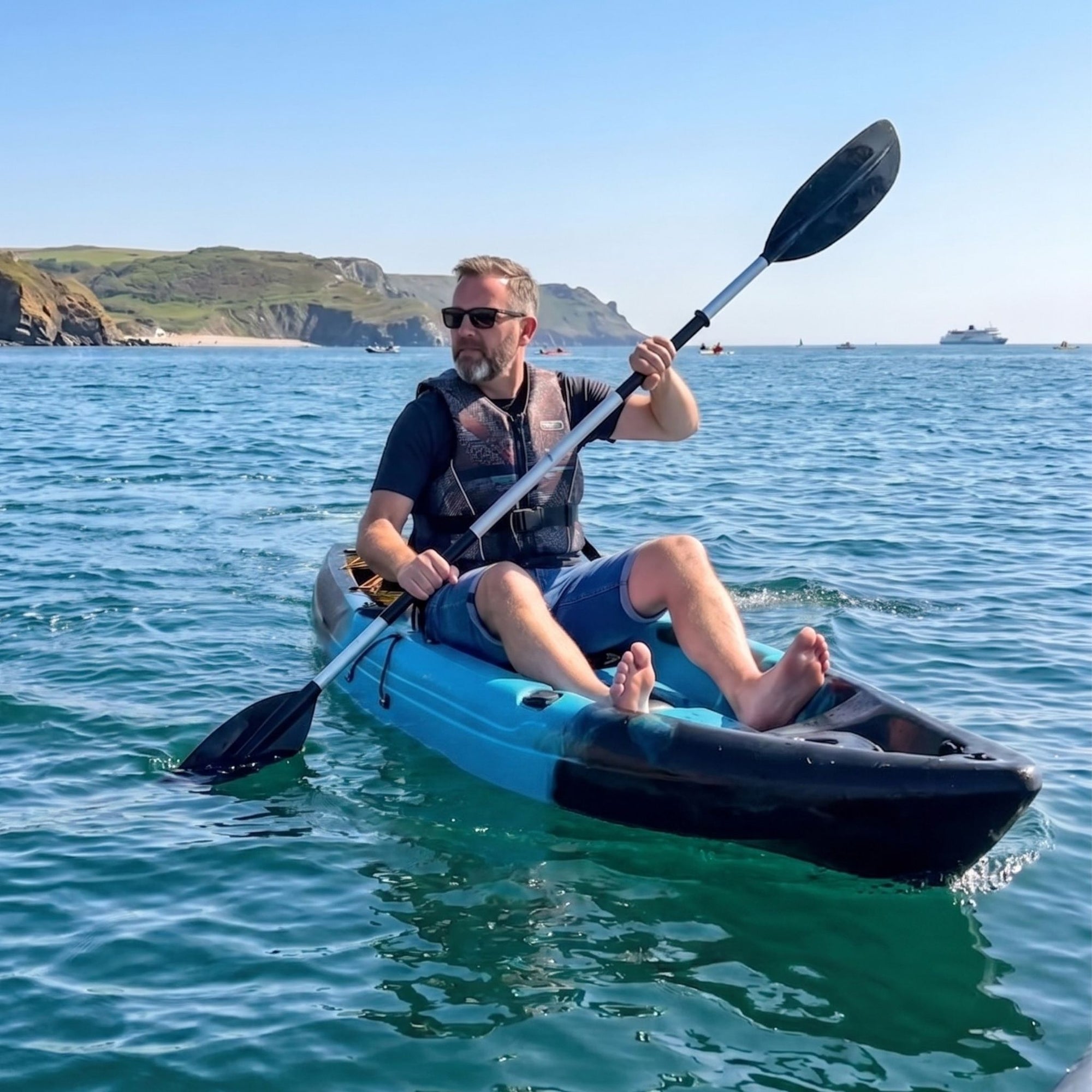 Man paddling single sit on top kayak on calm sea near UK coastline